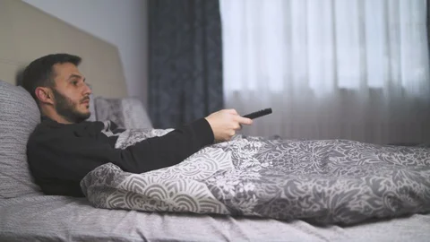 Sick man lying bed watching TV switching channels with remote Stock Footage 129325007