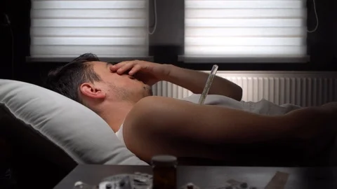 Sick man lying on bed.Checks temperature Stock Footage 125809893