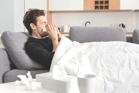 Sick man lying on sofa and blowing nose 스톡 사진