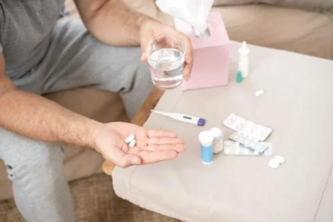Sick man lying on sofa checking his temperature at home in the living room. M Stock Photos
