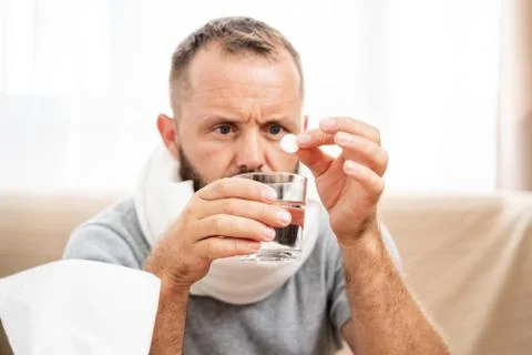 Sick man lying on sofa checking his temperature at home in the living room. M Stock Photos