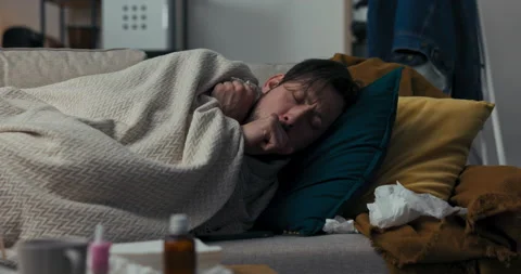 Sick man is lying on sofa, covered with blanket. He is not feeling well and is Vídeo Stock 218329856