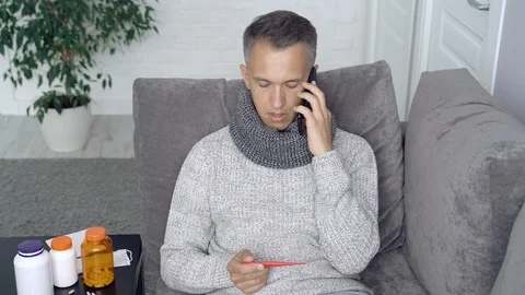 Sick man measuring body temperature and calling the doctor at home Stock Footage 111581831