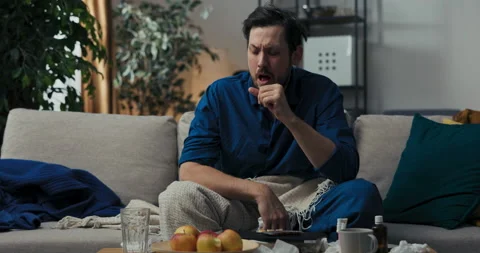 Sick man in pajamas is sitting on sofa. He covered with blanket because he has Vídeo Stock 218327684