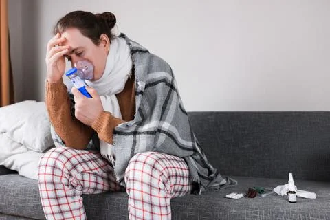 Sick man in pajamas using nebulizer mask for inhalation and holding head in.. Stock Photos