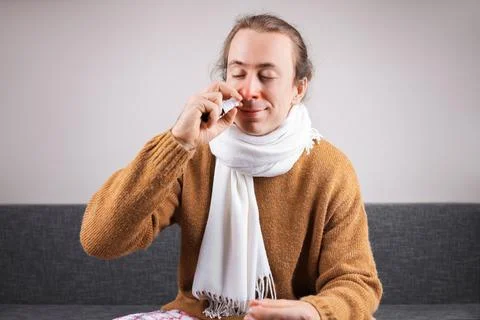Sick man with red nose using nasal spray to treat runny nose and congestion.. Stock Photos