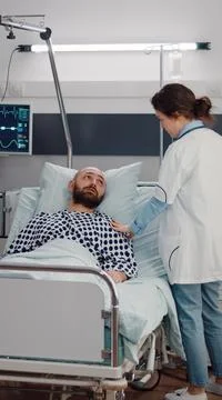 Sick man resting in bed while therapist doctor monitoring respiratory recovery 库存照片