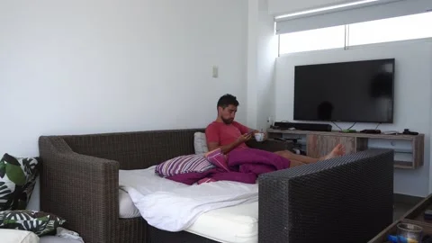 A sick man sitting on the couch having a coffee in the morning and looking at Stock Footage 193076282