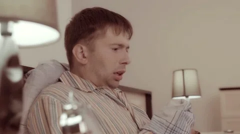 Sick man sitting in his bed and sneezing sharply Видео 68421030