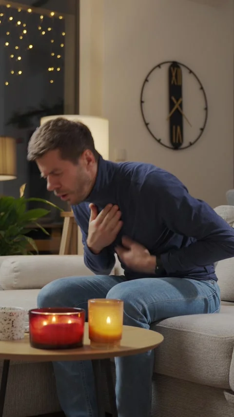 Sick man sitting on sofa holding chest with pain at home Stock Footage 326281299