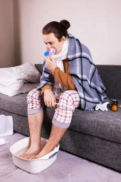 Sick man treating flu with nebulizer mask and soaking feet in hot water on .. Foto stock