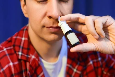 Sick man using a nasal spray for cold and flu treatment. Applying medicine .. Stock Photos