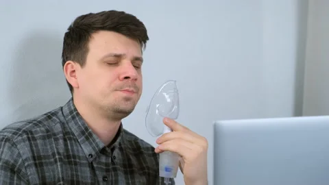 Sick man is using nebulizer and inhaler for treatment cure working on laptop. Stock Footage 152715882