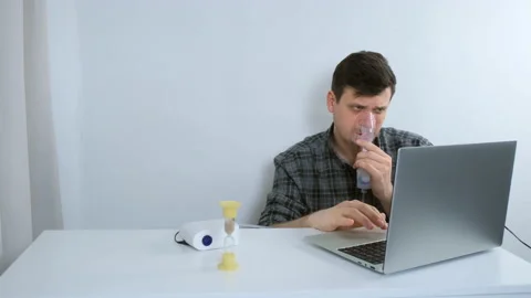 Sick man is using nebulizer and inhaler for treatment cure working on laptop. Stock Footage 158436402