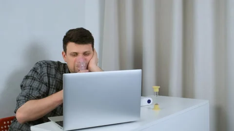 Sick man is using nebulizer and inhaler for treatment cure working on laptop. Stock-Footage 159485851