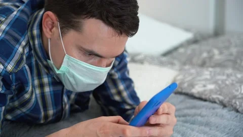 Sick man wear protective face mask, lay on bed, browsing internet. Isolation Stock Footage 131479293