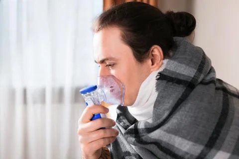 Sick man wrapped in blanket using nebulizer mask for respiratory inhalation.. Stock Photos