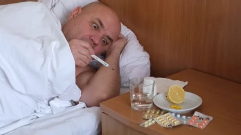 Sick middle aged man with fever lying on bed, looks at thermometer and surprised Video stock 301372607