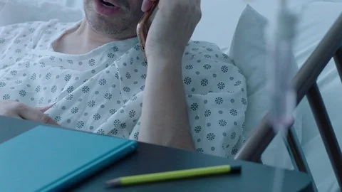 A sick middle aged man with an IV drip talking on the phone in a hospital bed, Stock Footage 74388355