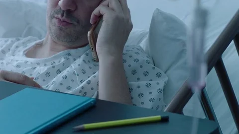 A sick middle aged man with an IV drip talking on the phone in a hospital bed, Stock Footage 74391036