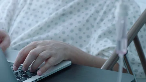 A sick middle aged man with an IV drip typing on a laptop computer in a hospital Stock Footage 74399490