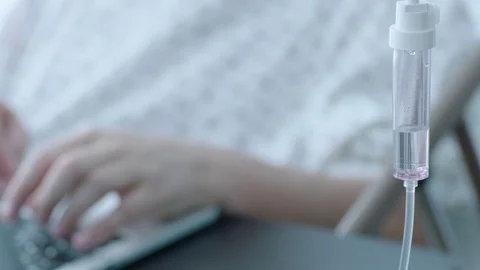 A sick middle aged man with an IV drip typing on a laptop computer in a hospital Stock Footage 74401339