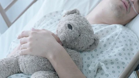 A sick middle aged man on oxygen holding a teddybear in a hospital bed, slow Stock Footage 74377917