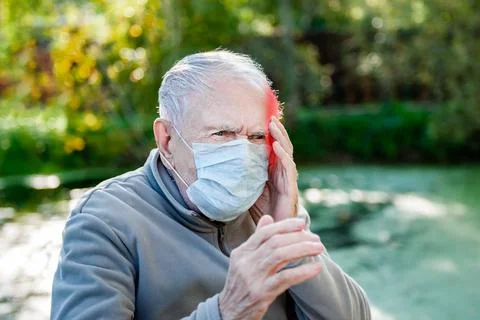 Sick old gray-haired man sits in a medical mask. Men have headaches. concept Stock Photos