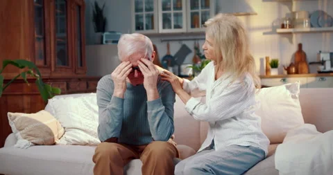 Sick old man feeling pain in head sitting on sofa at home, mature woman near Stock Footage 306469615