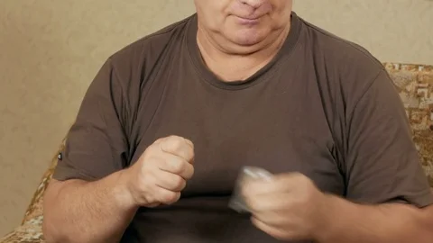 Sick senior overweight man taking pills in house on a sofa and drinks water in a Stock Footage 71244326