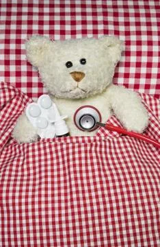 Sick teddy bear lying in a red checked bed. concept for illness. Stock Photos