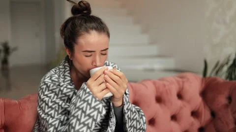 A sick woman drinks tea while sitting under a blanket and coughs. Stock Footage 252466686
