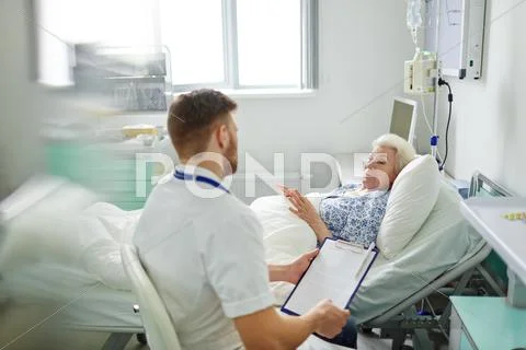 Sick woman lying in hospital bed and talking to doctor Stock Photos