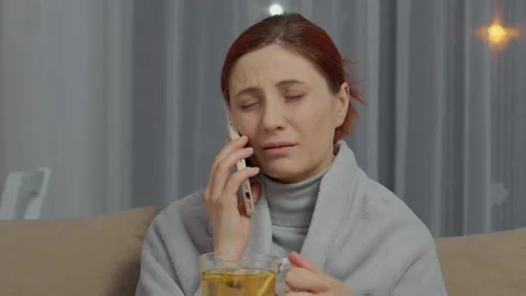 Sick woman talks on the phone while sipping herbal tea for recovery Stock Footage 346706360