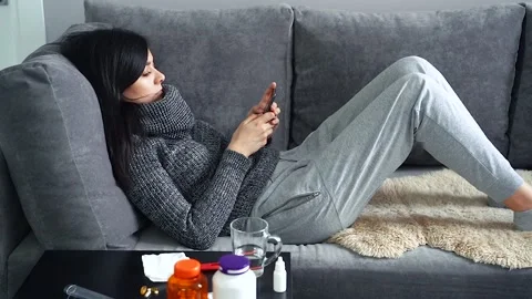 Sick woman using smartphone while lying on the couch at home Stock Footage 100288517
