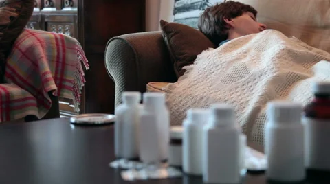 Sick young man on couch with flu and a blanket taking medication Stock Footage 51677081