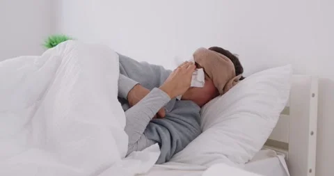 Sick young man lying on bed in bedroom suffering from runny nose and temperature Stock Footage 283763490
