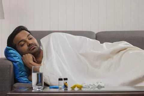 A sick young man lying on sofa while suffering from fever Stock Photos