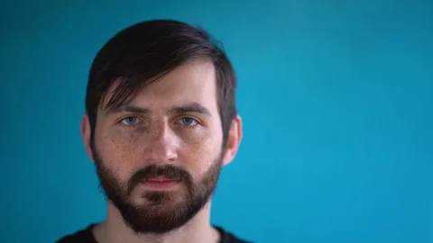 Sick young man puts on face mask close up. Ill bearded guy on blue background Video stock 129979080