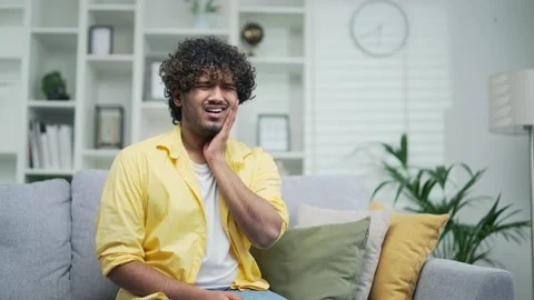 Sick young man suffers from a severe toothache Cavity while sitting on the sofa  Stock Footage 235487777
