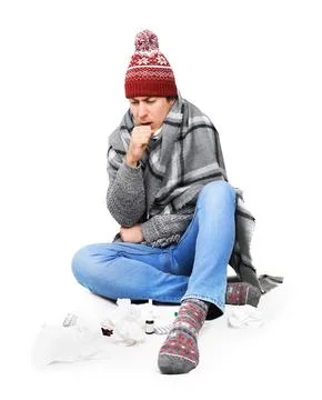 Sick young man in winter hat coughing while sitting on floor with medicines.. Stock Photos