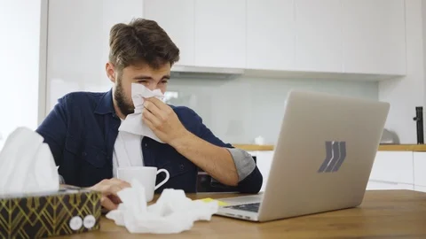 Sick young man working on laptop at home blowing his nose Stock Footage 119313473