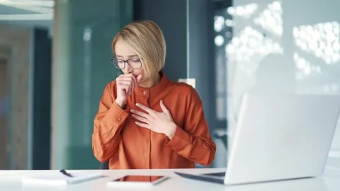 Sick young woman coughing while working on a laptop while sitting at a workplace Stock Footage 239026488