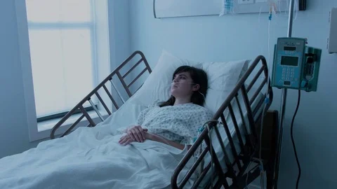 A sick young woman with an IV recovering in a hospital bed next to a window, Stock Footage