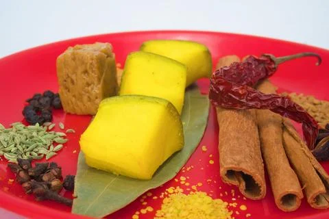 Side and close-up view of several spices on a red plate and chunks of raw mango Stock Photos