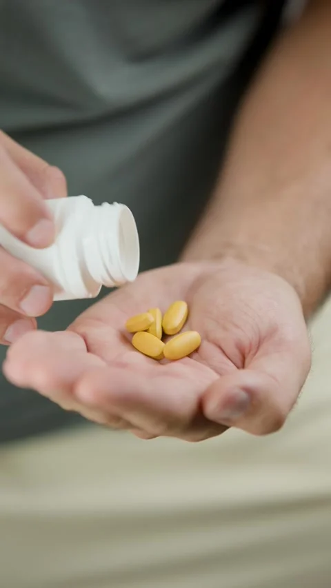 Side Angle of Man Pouring Yellow Capsules Into Hand Close Up Video stock 343450767