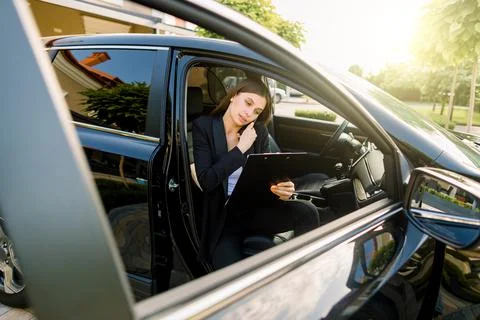 Side angle view of young pretty businesswoman, sitting inside her car on Stock-Fotos