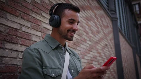 Side attractive young Caucasian man with headphones using cell phone leaning Stock Footage 266567997