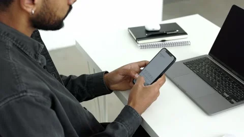 Side Back view shot black bearded man sitting at the white desk texting on cell Stock Footage 196127237