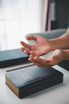 Side close-up of open hands raised above a Holy Bible during personal praye.. Stock Photos